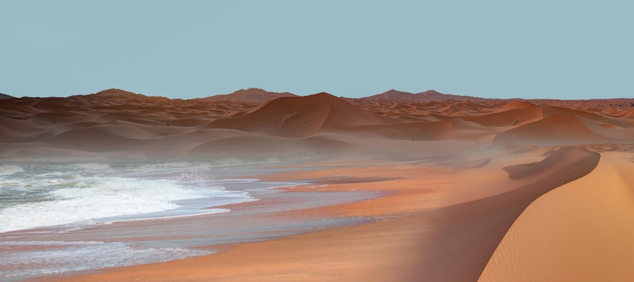 Un paysage surréaliste mêle désert et océan dans le désert de Namib en Namibie, avec des dunes de sable ondulantes qui se fondent dans les vagues déferlantes sous un ciel clair.